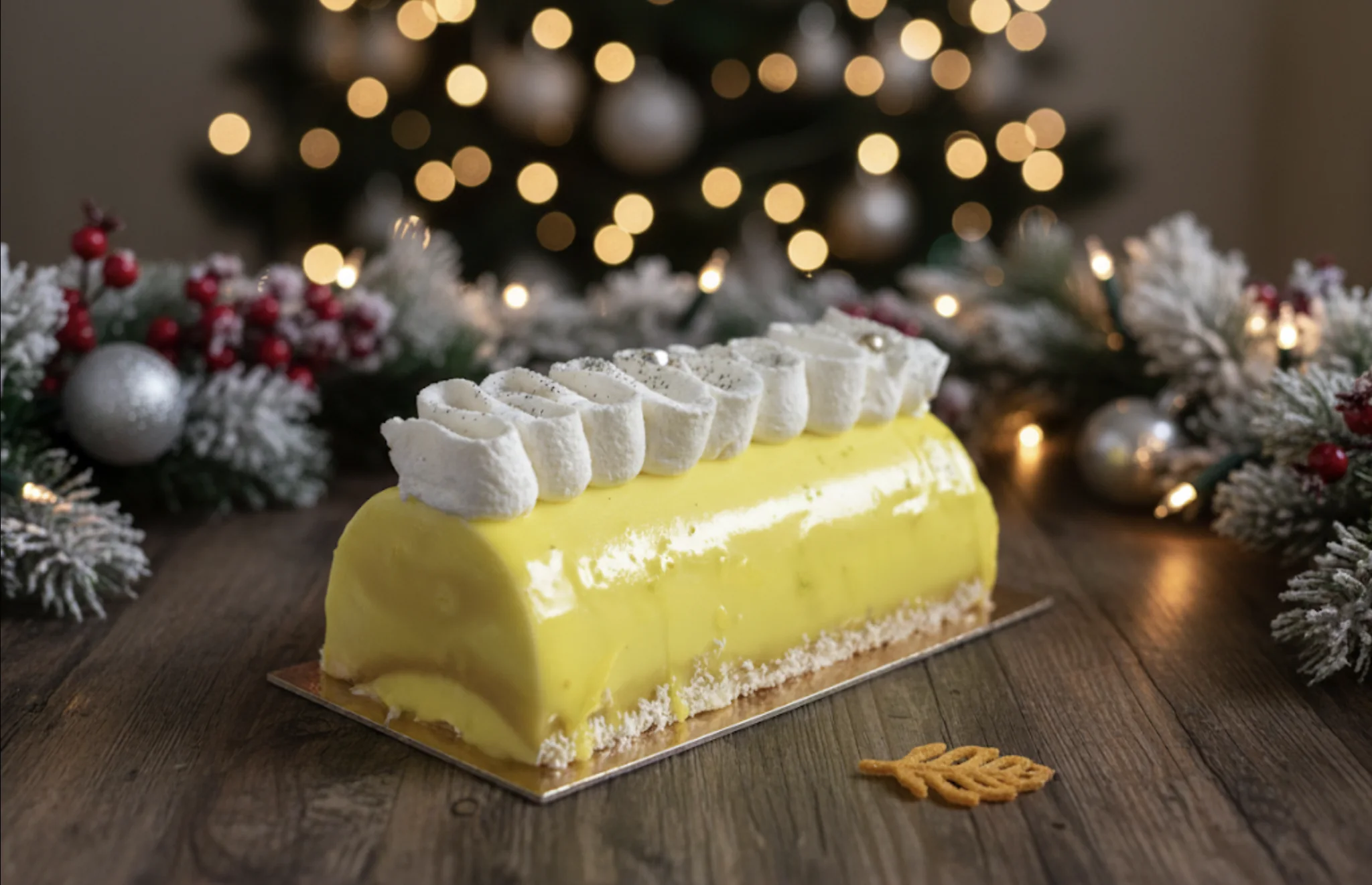 Patisserie restaurant Martigny Une bûche couleur citron, avec une colerette de crème et des perles dorées, devant un sapin de noël